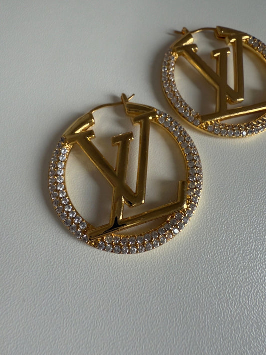 Gold earrings with circular design and embedded stones on a light gray background