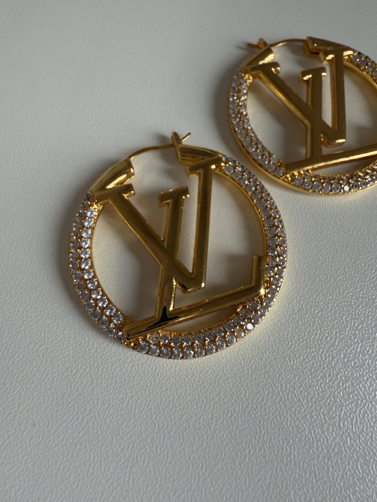 Gold earrings with circular design and embedded stones on a light gray background